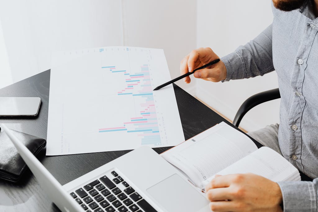 An office setup with a person analyzing a graph printout while using a laptop and notebook.