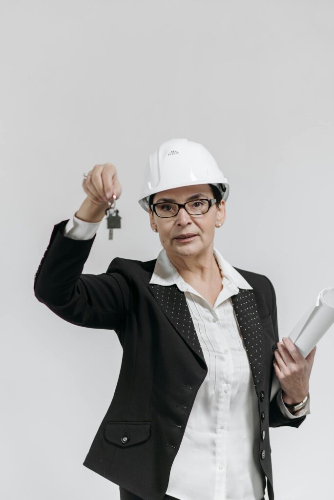 Professional female real estate agent in a suit holding keys and documents against a white background.